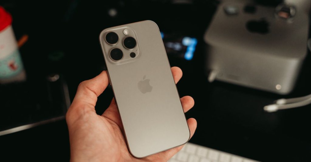 A hand holding a sleek smartphone in a tech-savvy office environment, showcasing its design.