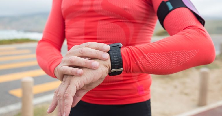 A person in red activewear checks their wristwatch during an outdoor exercise session.