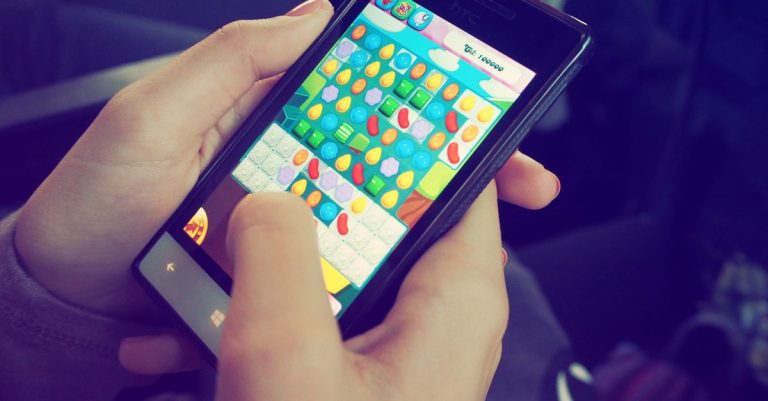 Hands holding a smartphone with a colorful puzzle game on the screen, displaying modern technology.