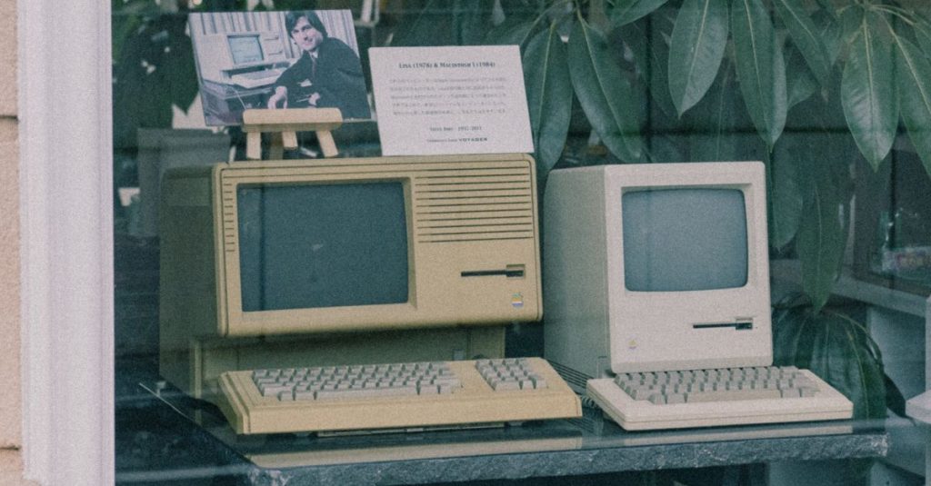 Retro Apple computers with keyboards displayed in a Tokyo store window, showcasing early tech design.