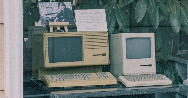 Retro Apple computers with keyboards displayed in a Tokyo store window, showcasing early tech design.