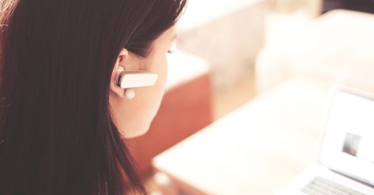 A businesswoman using a Bluetooth headset while working on her laptop in a modern office.
