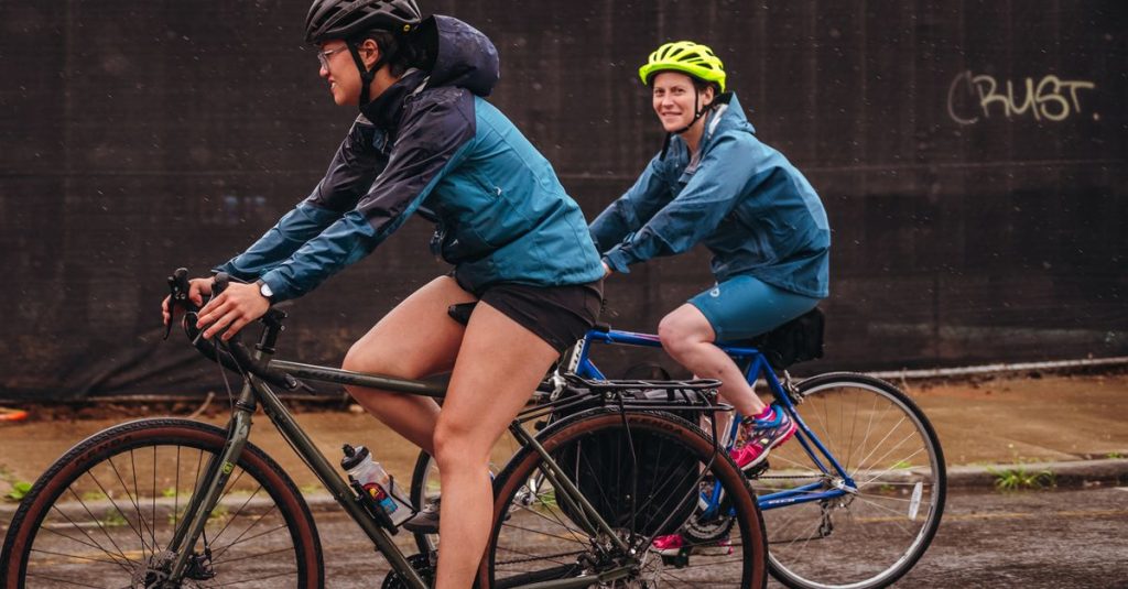 Two women in activewear biking on a rainy street, showcasing outdoor fitness.