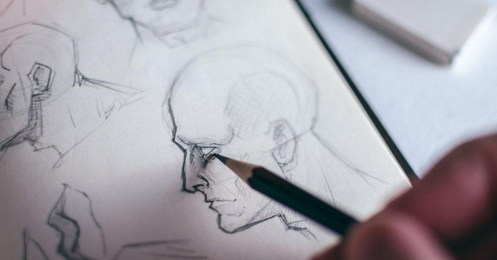 Detailed image of a hand sketching a human face in a sketchbook, emphasizing creativity.