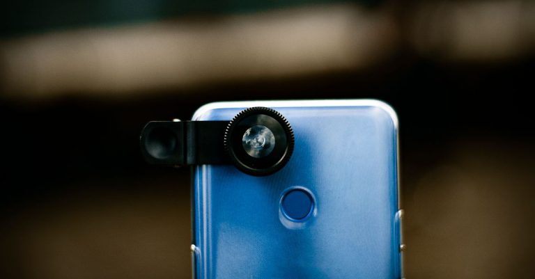 Zoom optical lens attached to camera of modern smartphone against blurred background in daytime