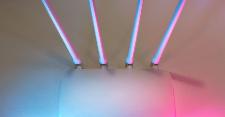 Sleek white wireless router with four antennas emitting soft blue and pink light.