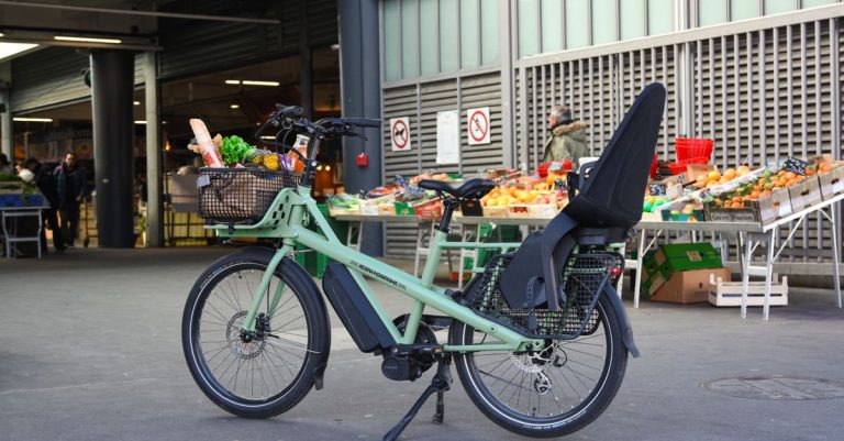 Electric cargo bike loaded with groceries parked outside a market in France, showcasing green urban mobility.