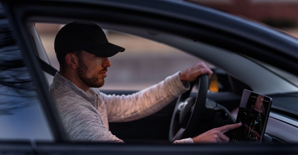A man interacts with a touchscreen inside an electric car, driving through Dallas, TX.