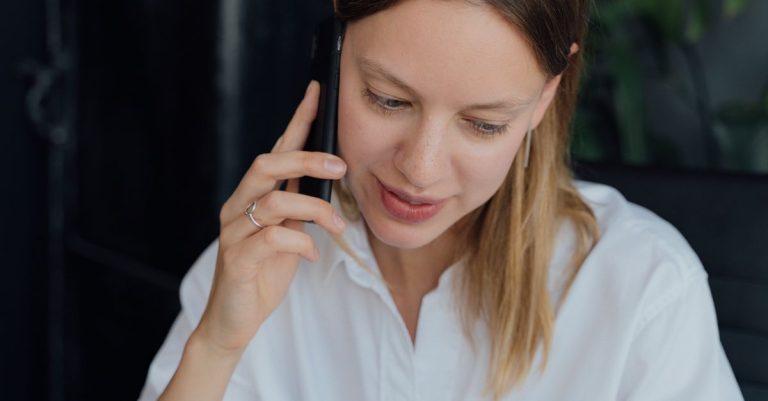 A professional woman in a white shirt making a phone call in an indoor setting, showing communication and business engagement.