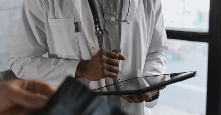 A professional medical practitioner holding a tablet, focused on work in a clinical setting.