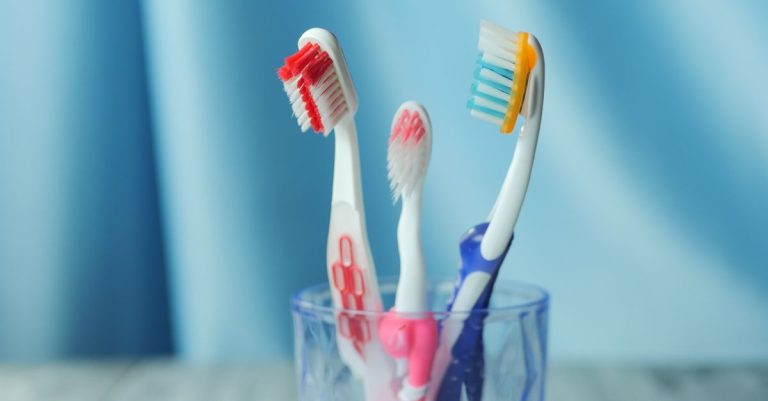 A trio of vibrant toothbrushes in a glass on a blue background, emphasizing dental hygiene.