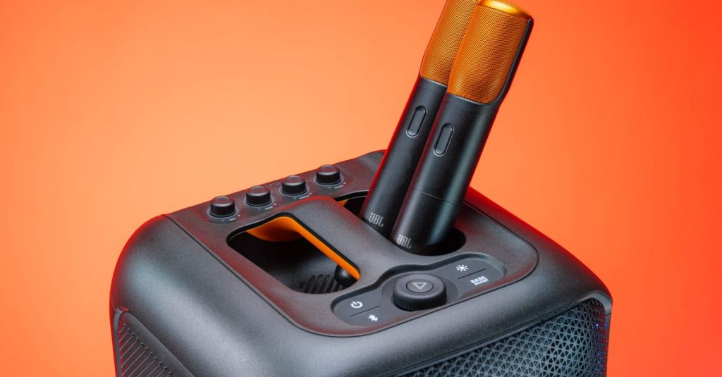Modern JBL speaker featuring two wireless microphones, set against a vibrant orange background.