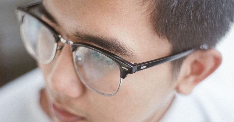 A detailed close-up of a young man wearing eyeglasses, focusing on his face and eyewear.