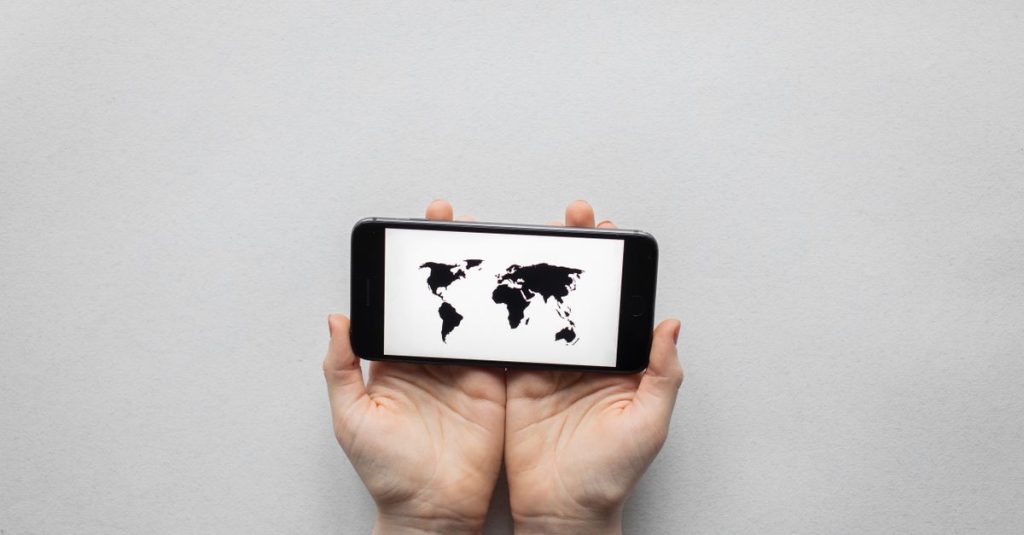 Hands holding a smartphone displaying a world map on a white background.