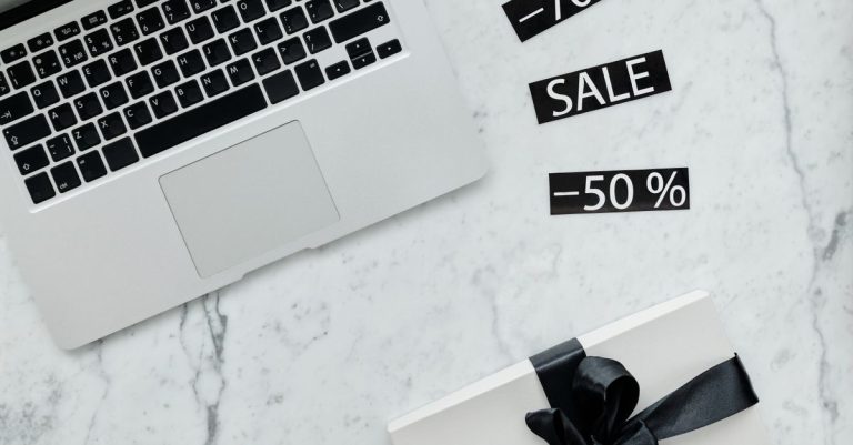 Marble workspace with a laptop, gift box, and sale tags offering discounts.
