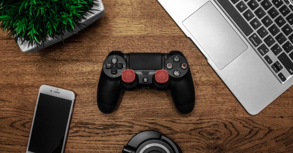 A flat lay photo showcasing a gaming console, laptop, smartphone, and headphones on a wooden tabletop.