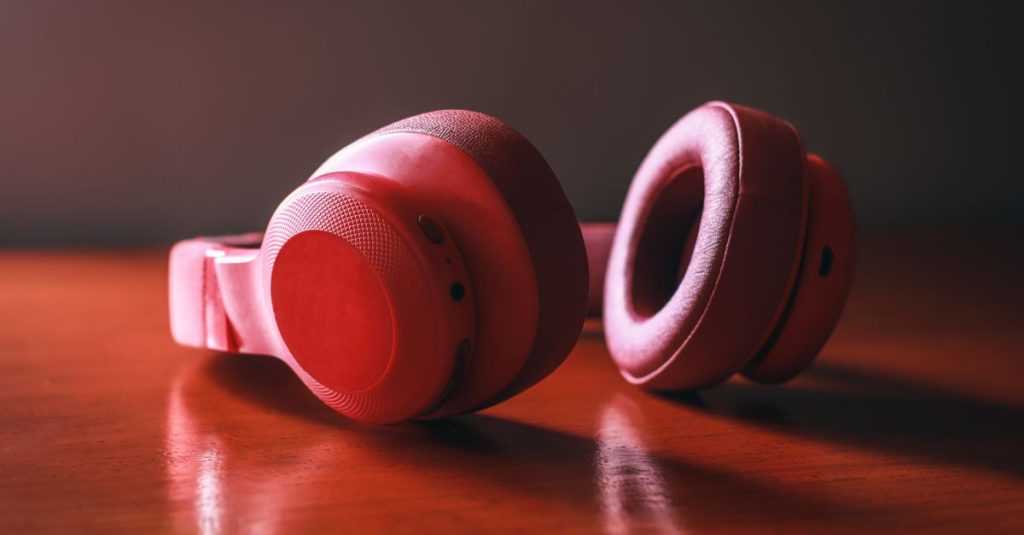 Close-up of red wireless headphones resting on a wooden surface, highlighting sleek design and vibrant color.