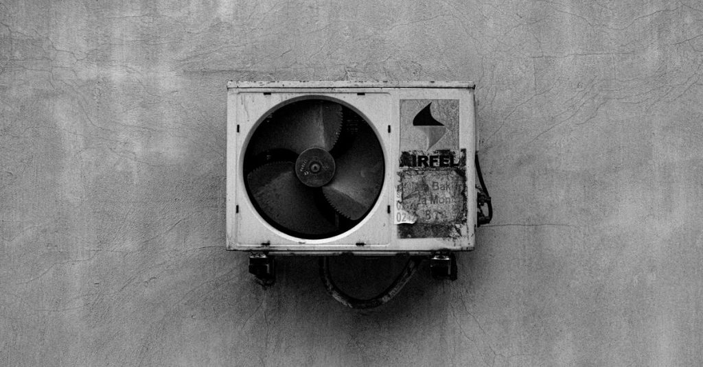 Monochrome image of a wall-mounted air conditioner on a concrete surface.
