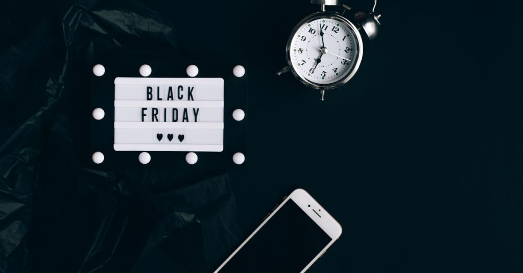 Stylish Black Friday promotion with alarm clock and smartphone on dark background.
