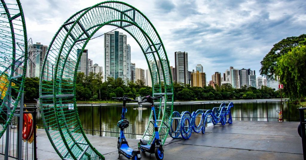 Scooters parked among urban art installations by a lake in Londrina, Brazil.