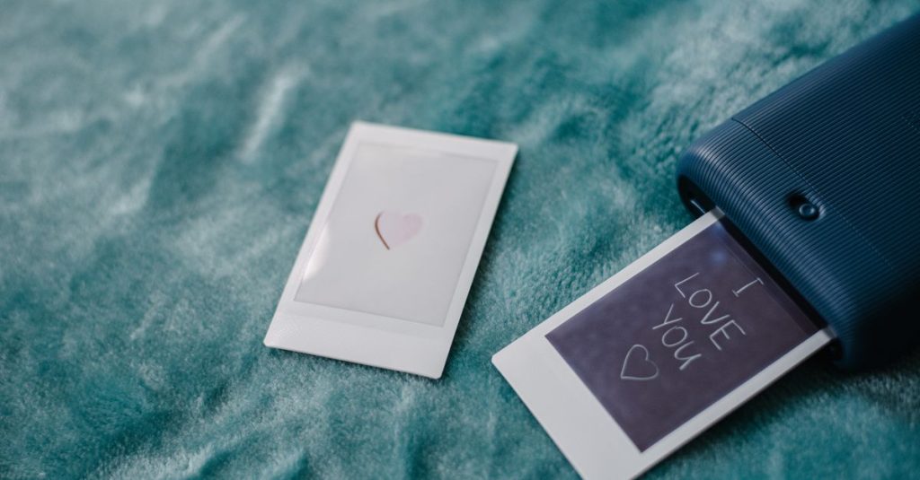 From above of contemporary instant camera printing photography with I Love You title on soft plaid