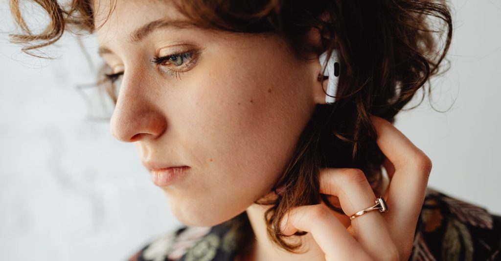 Close-up of a woman with curly hair listening to music using AirPods, showcasing technology and lifestyle.