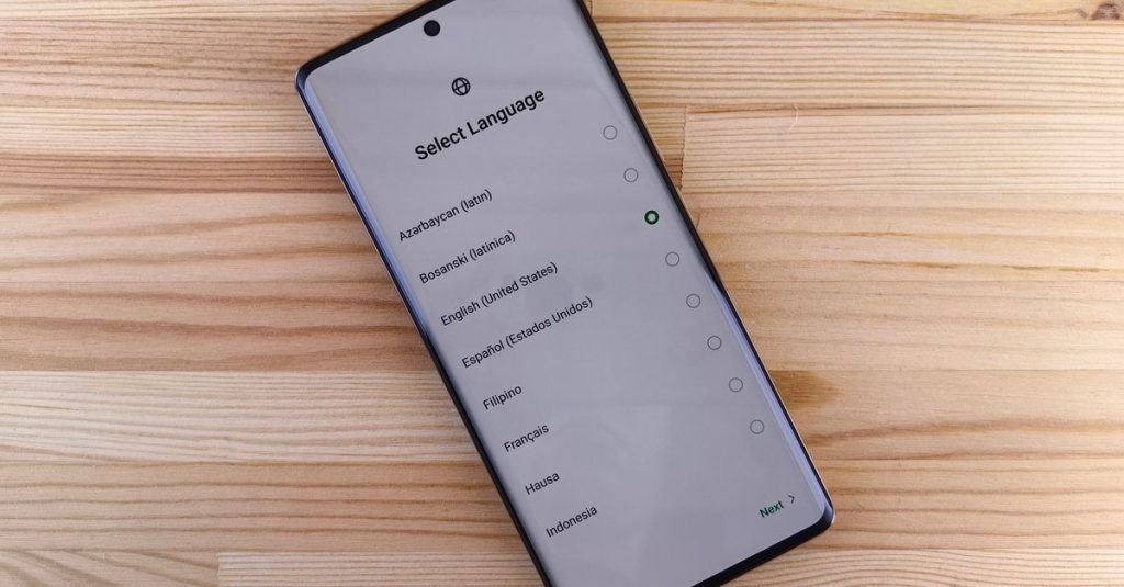 Close-up of smartphone with language selection screen on wooden table.
