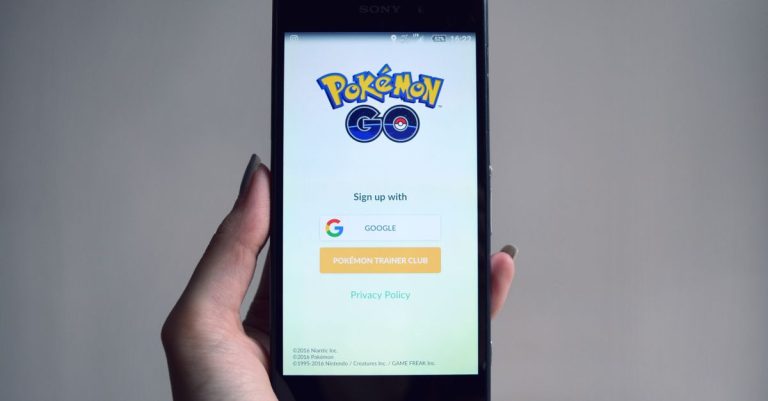 Smartphone displaying Pokémon Go app sign-in screen, held in hand.