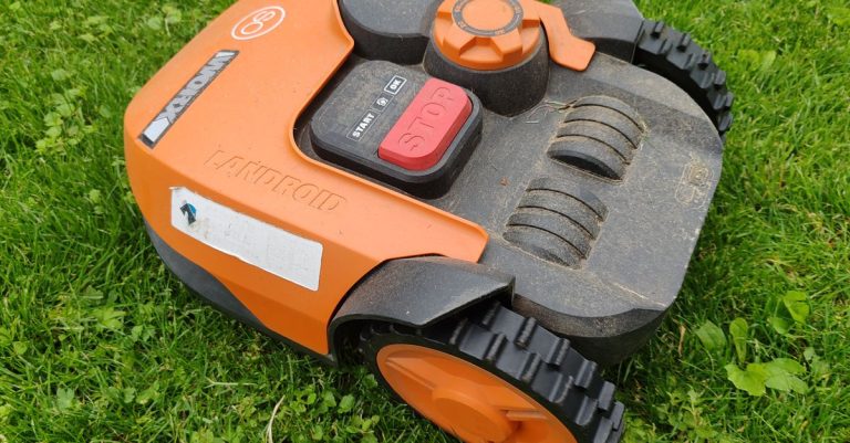 A modern robotic lawn mower in vibrant orange resting on a green lawn, ready for automated mowing tasks.