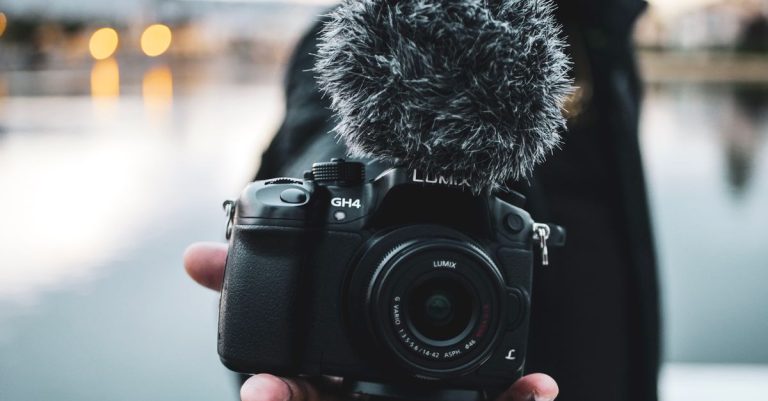 Close-up of a DSLR camera with a microphone held in hand outdoors, blurred background.