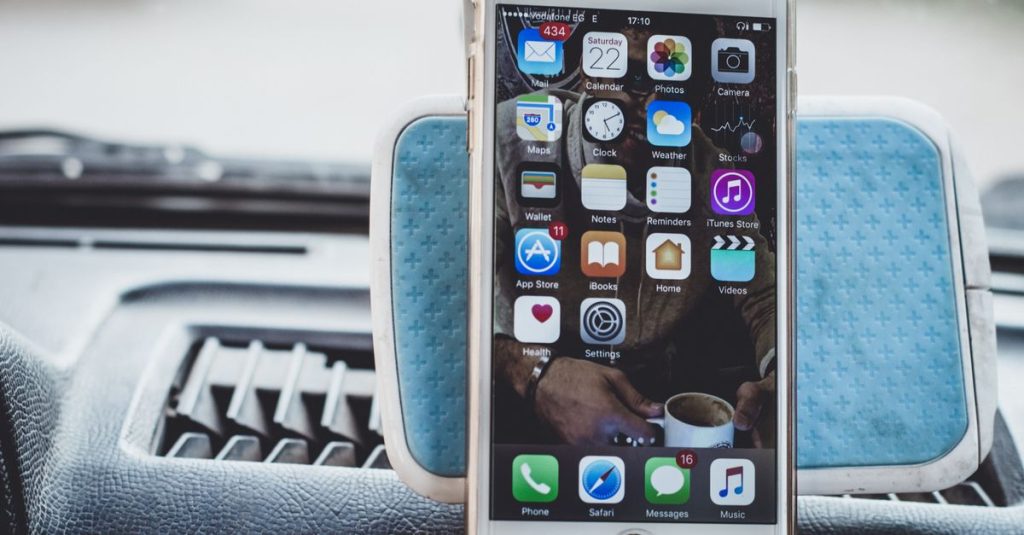 Close-up of a smartphone mounted on a car dashboard showing home screen with apps.