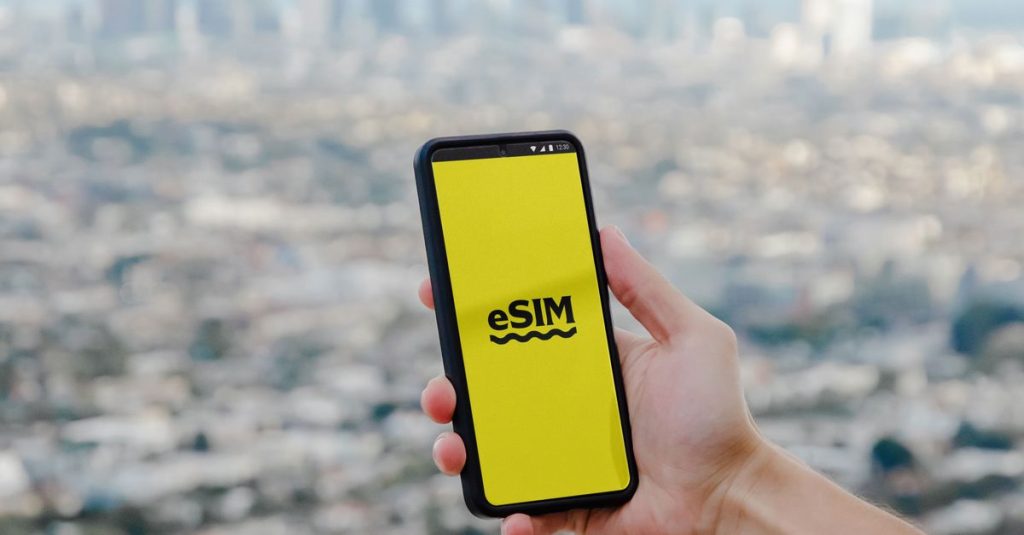 Hand holding a smartphone showcasing eSIM technology with a blurred Los Angeles skyline in the background.