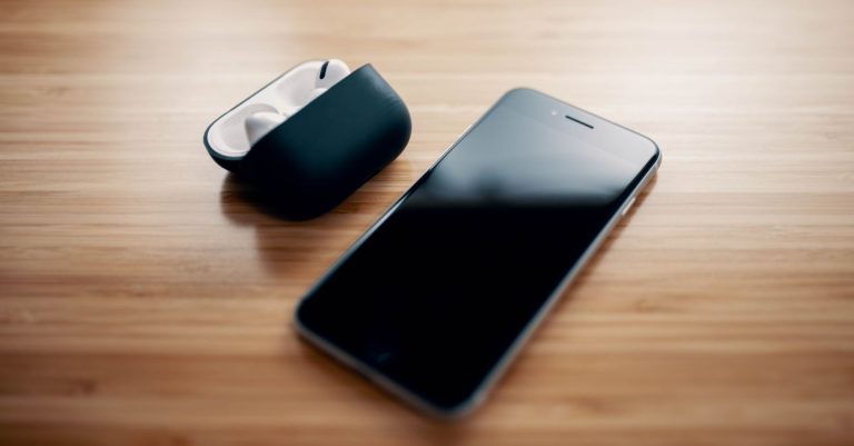 High angle of black modern smartphone and TWS earbuds on black charging case on wooden table