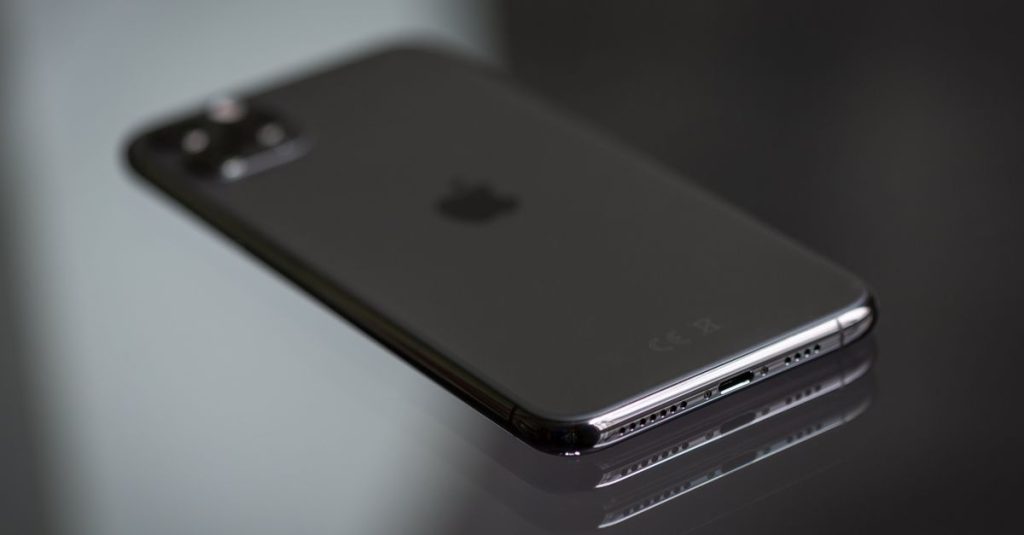 Close-up of a black smartphone on a shiny reflective surface, highlighting its sleek design.