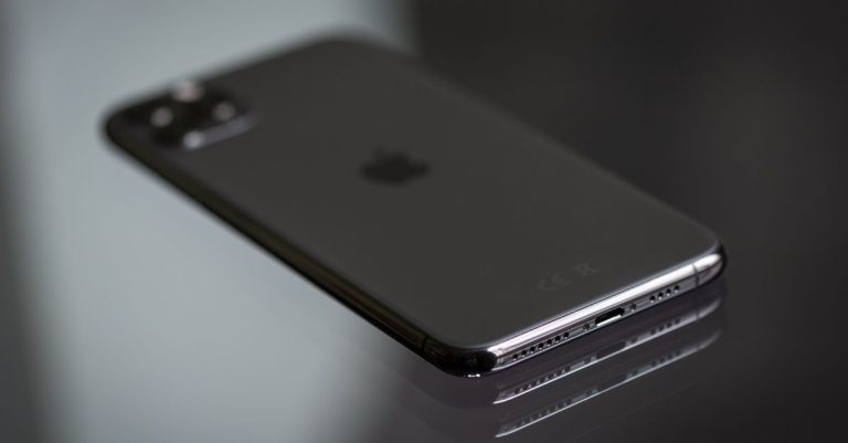 Close-up of a black smartphone on a shiny reflective surface, highlighting its sleek design.