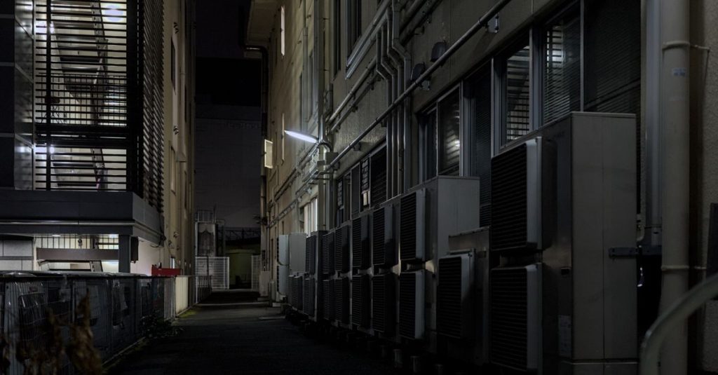 A dimly lit urban alley in Kyoto featuring air conditioning units, captured at night.