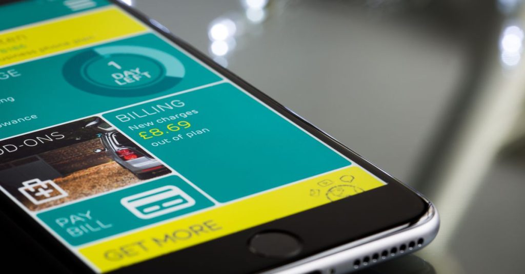 Close-up of a smartphone displaying a billing app interface on a reflective surface.