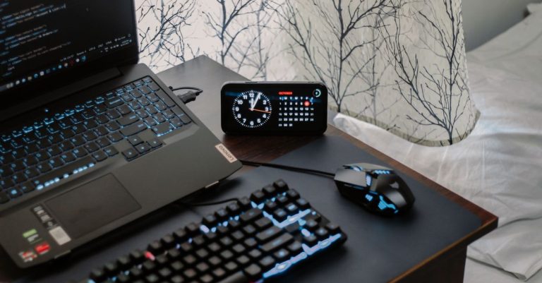 A modern workspace featuring a laptop, digital clock, gaming mouse, and keyboard, ideal for work and tech enthusiasts.