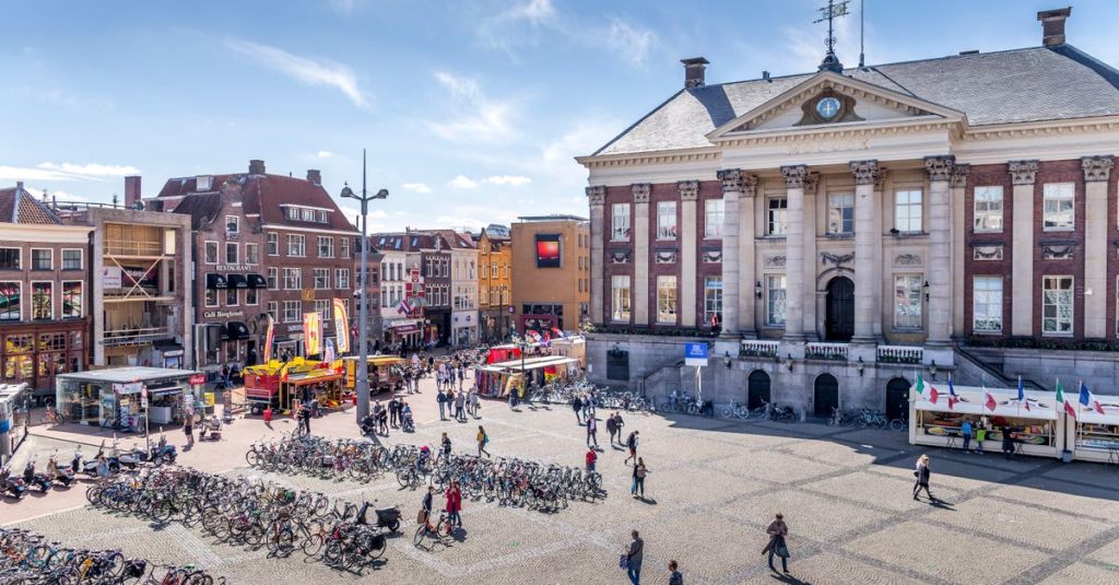 Vibrant scene at Grote Markt in Groningen with bicycles and walking pedestrians on a sunny day.