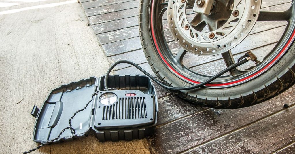 Close-up of a motorcycle tire being inflated using a portable air pump.