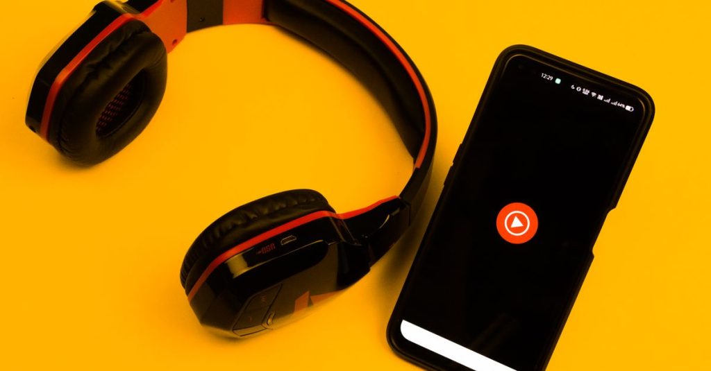 Wireless headphones and smartphone with play icon on a vibrant yellow background.