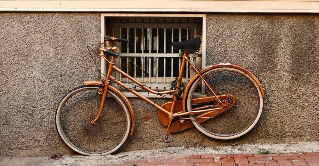 A vintage rusty bicycle leaning against a weathered urban wall with a barred window.
