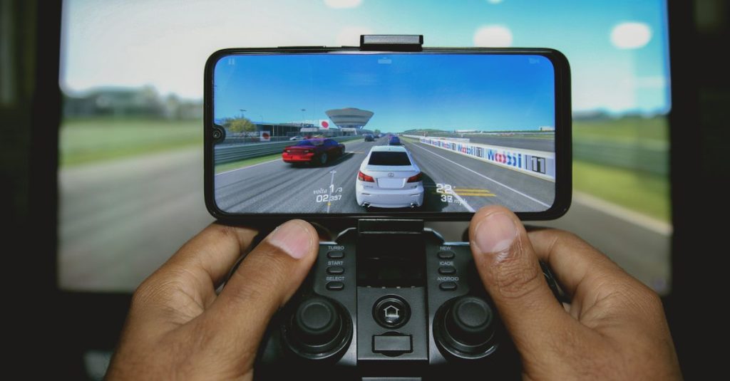 Close-up of hands playing a racing game on a mobile device with a controller.