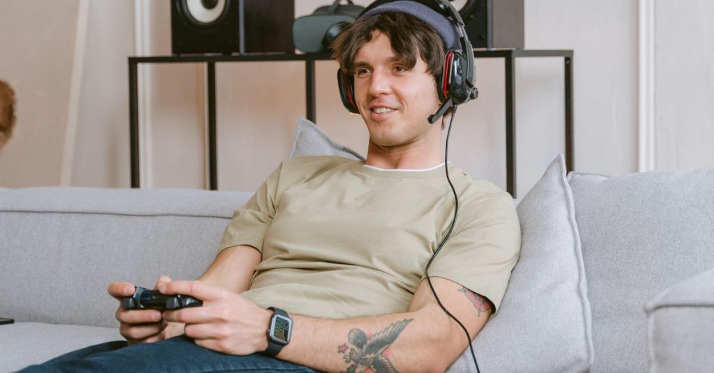 Young man enjoying video gaming session at home with a headset and controller.
