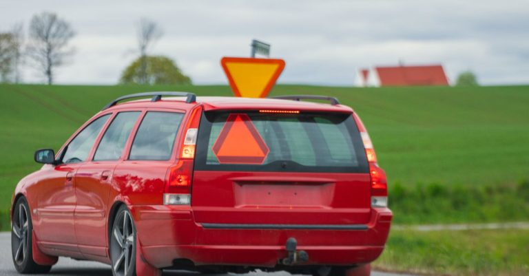 A red car drives on a countryside road in Jönköping, Sweden with a rural landscape.
