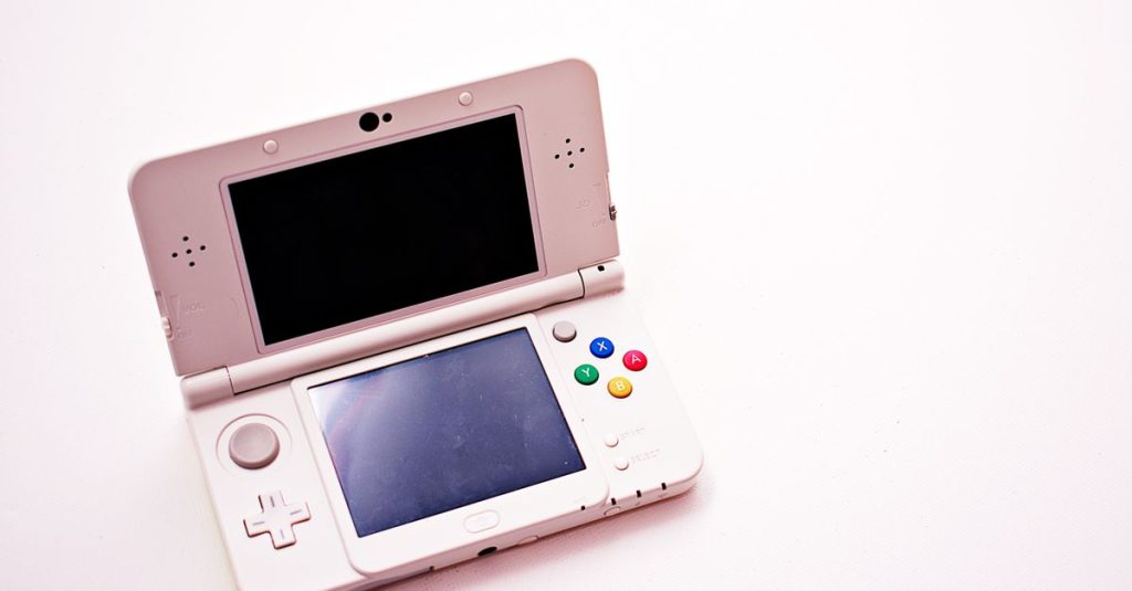 A clean shot of a white portable gaming console with two screens.