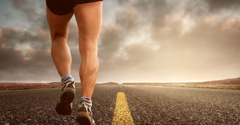 Runner's legs on a road during a sunset, symbolizing endurance and outdoor fitness training.