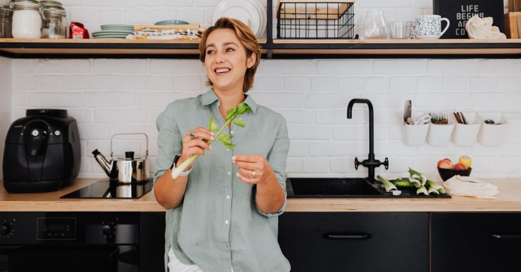 Smiling woman with vegetables in a stylish kitchen showcasing modern interior design.