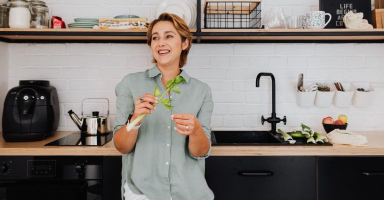 Smiling woman with vegetables in a stylish kitchen showcasing modern interior design.