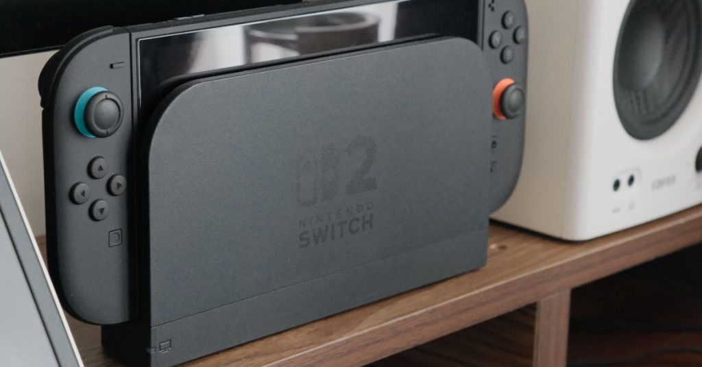Nintendo console docked among speakers and a monitor on a wooden shelf.
